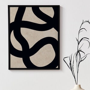 Könnte beinhalten: Abstrakter Kunstdruck in einem schwarzen Rahmen. Das Kunstwerk zeigt dicke, schwarze, geschwungene Linien auf beigem Hintergrund. Ein kleiner, runder, beiger Behälter mit Deckel liegt auf einem schwarzen Buch. Eine weiße Vase mit kreisförmiger Öffnung hält schwarze Stiele.
