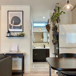 Puede incluir: Un refrigerador blanco con una mesa y sillas negras delante. Hay una estanter&iacute;a negra con una impresi&oacute;n abstracta en blanco y negro colgada en la pared sobre la mesa. Hay plantas colgando del techo sobre el refrigerador.