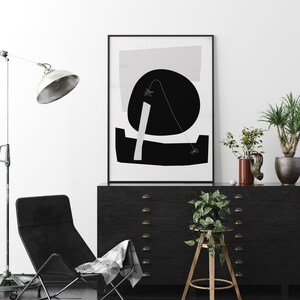Puede incluir: Impresi&oacute;n de arte abstracto en blanco y negro en un marco negro que cuelga sobre una c&oacute;moda negra con cajones. Una silla negra con una manta de patr&oacute;n blanco y negro est&aacute; en primer plano. Una planta en maceta est&aacute; en un taburete de madera.
