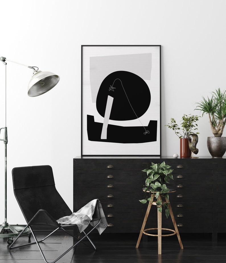 Puede incluir: Impresi&oacute;n de arte abstracto en blanco y negro en un marco negro que cuelga sobre una c&oacute;moda negra con cajones. Una silla negra con una manta de patr&oacute;n blanco y negro est&aacute; en primer plano. Una planta en maceta est&aacute; en un taburete de madera.