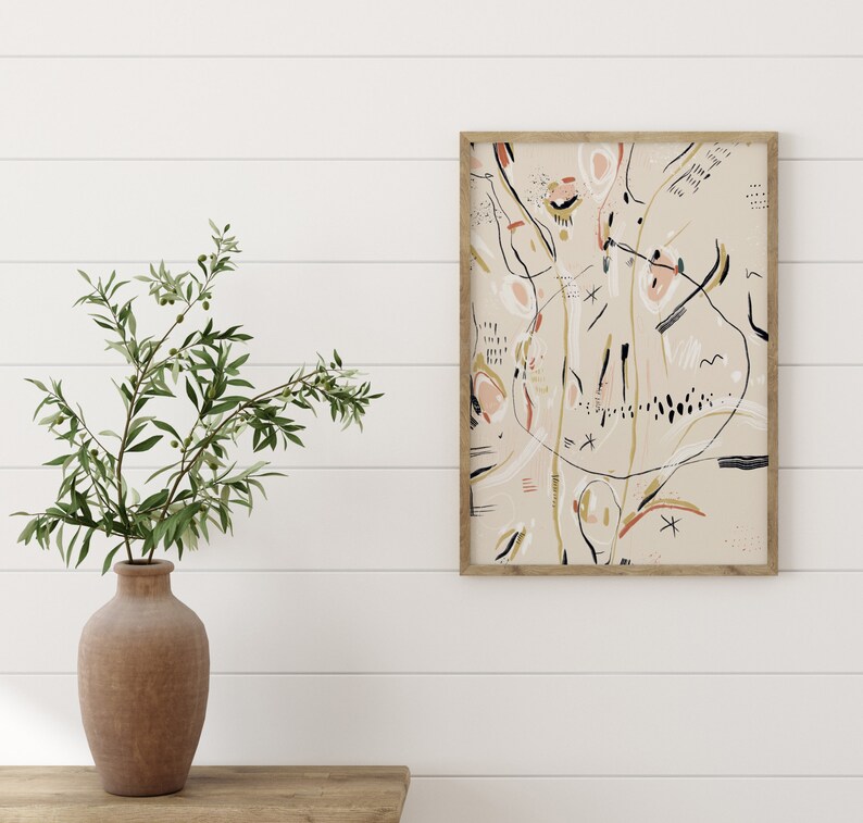 May include: A framed abstract art print with a beige background and black, white, pink, and gold lines and shapes.