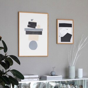 May include: Two framed abstract art prints with geometric shapes in black, white, and gray on a white background. The prints are hanging on a gray wall.