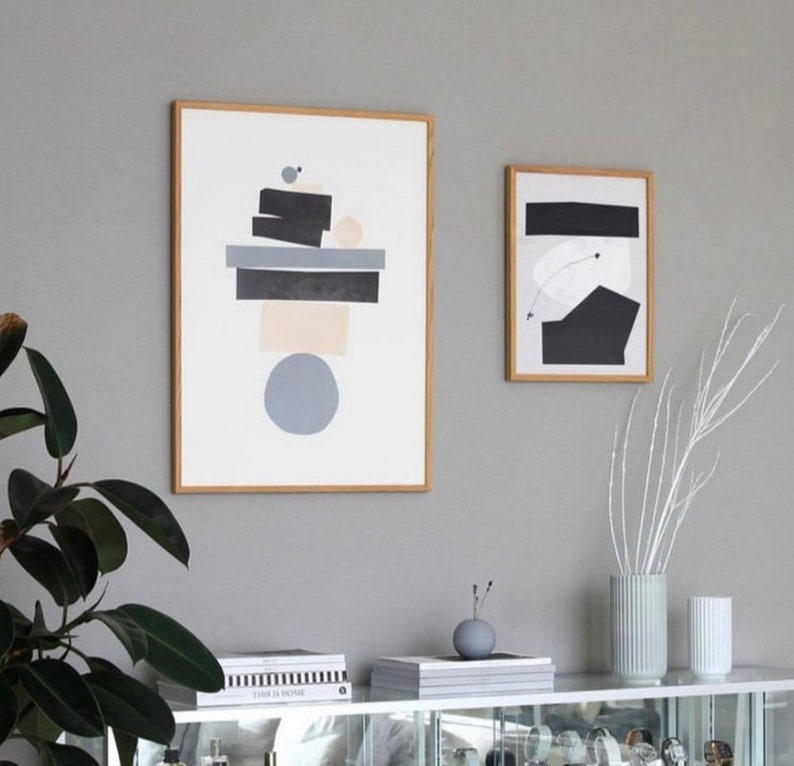 May include: Two framed abstract art prints with geometric shapes in black, white, and gray on a white background. The prints are hanging on a gray wall.