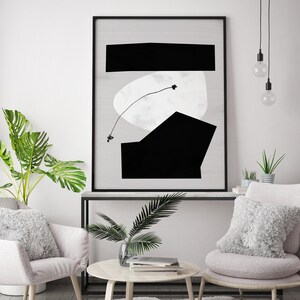 May include: A black and white abstract art print in a black frame hangs above a white console table with a potted plant and two armchairs with fluffy white pillows. The room has a white wall and a light wood floor.