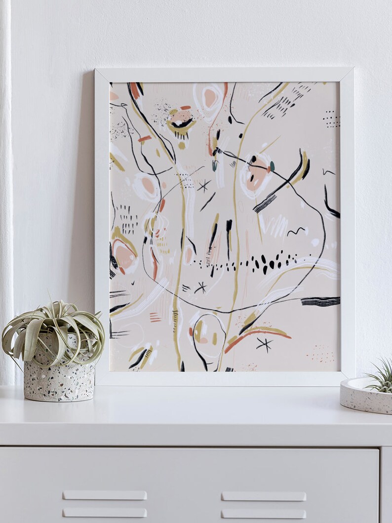 May include: A framed abstract art print with a beige background and black, white, pink, and gold lines and shapes.