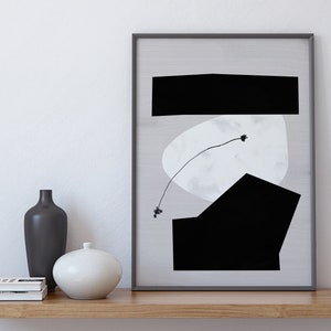 May include: A black and white abstract art print in a black frame, with a white background and black geometric shapes. The print is on a wooden shelf with two vases and a stack of books.