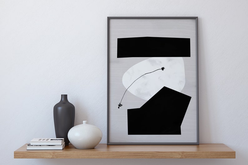 May include: A black and white abstract art print in a black frame, with a white background and black geometric shapes. The print is on a wooden shelf with two vases and a stack of books.
