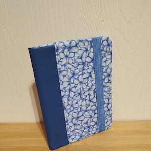 May include: A blue notebook with a white and blue floral pattern and a blue elastic band closure.