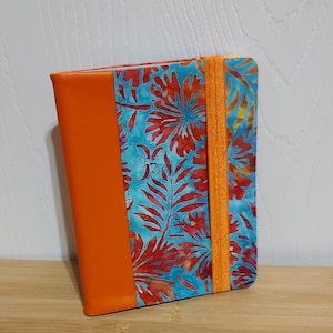 May include: A small orange and blue notebook with a floral pattern and an orange elastic closure.