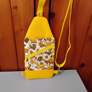 May include: A yellow crossbody bag with a zippered pocket and a pattern of cartoon bees and tigers. The bag has a yellow strap.