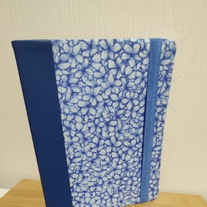 May include: A blue notebook with a floral pattern and a blue elastic closure.