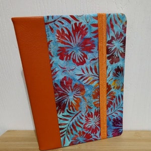 May include: A blue and red floral patterned notebook with an orange leather cover and an orange elastic closure.