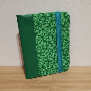 May include: A green leather notebook with a floral pattern and a turquoise elastic closure.
