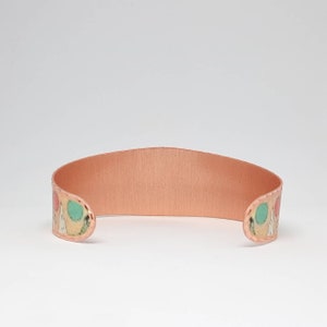May include: A copper bracelet with a colorful geometric pattern. The bracelet is open and has a smooth, polished finish.