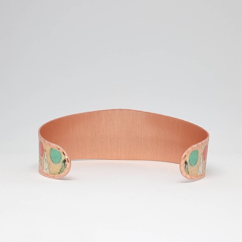 May include: A copper bracelet with a colorful geometric pattern. The bracelet is open and has a smooth, polished finish.