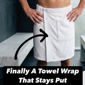 May include: A white towel wrap featuring a front pocket and a secure closure mechanism. The text "Finally A Towel Wrap That Stays Put" is displayed in white on a black rectangular background, accompanied by a black arrow pointing to the wrap.