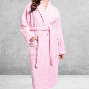 May include: A pink bathrobe with a shawl collar and a tie belt. The robe has two pockets on the front.