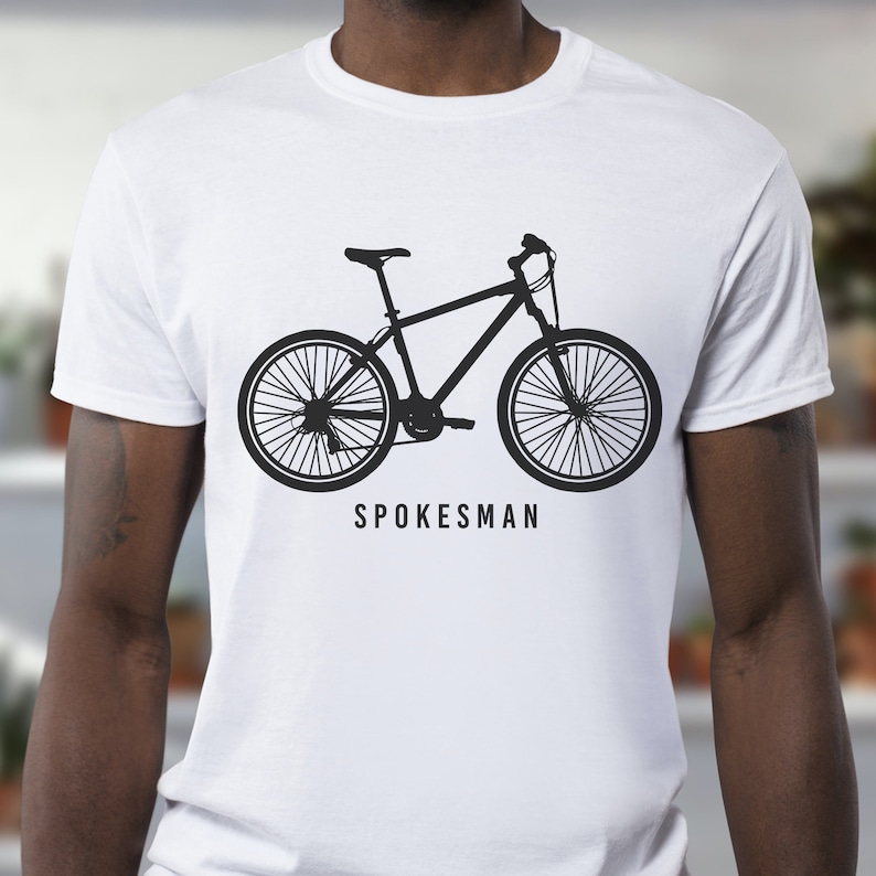 K&ouml;nnte beinhalten: Wei&szlig;es T-Shirt mit einer schwarzen Silhouette eines Fahrrads und dem Text "Spokesman" auf der Vorderseite.