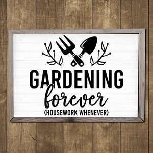 May include: A white sign with a black wooden frame, featuring a black silhouette of a gardening fork and trowel crossed over each other with green leaves on either side. The text reads "GARDENING forever (HOUSEWORK WHENEVER)"