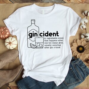 May include: White t-shirt with a black graphic of a bottle of gin, a glass of gin, a lime wedge, and ice cubes. The text "gincident" is written in black above the graphic. The text below the graphic reads: "A regrettable event that happens after one too many gins, usually occurring after gin o'clock."