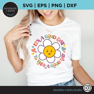 May include: A white t-shirt with a colorful graphic design featuring a smiling daisy with the text "It's a good day to have a good day".