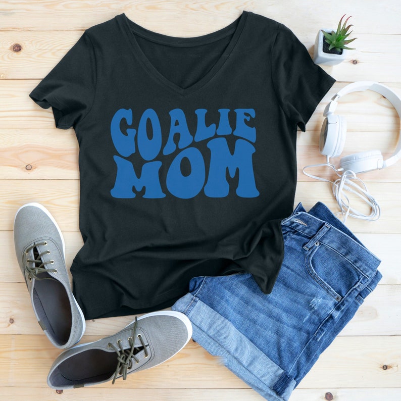 K&ouml;nnte beinhalten: Schwarzes T-Shirt mit V-Ausschnitt und dem Text "Goalie Mom" in blauen Retro-Lettern.