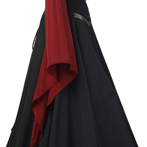 Puede incluir: Un vestido negro de estilo medieval con mangas largas. Las mangas son rojas y tienen un ribete dorado. El vestido tiene un corpi&ntilde;o ajustado y una falda fluida.