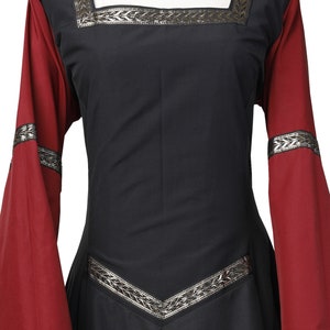 Puede incluir: Un vestido negro de estilo medieval con mangas largas. Las mangas son rojas con ribetes plateados. El vestido tiene ribetes plateados alrededor del escote y la cintura.