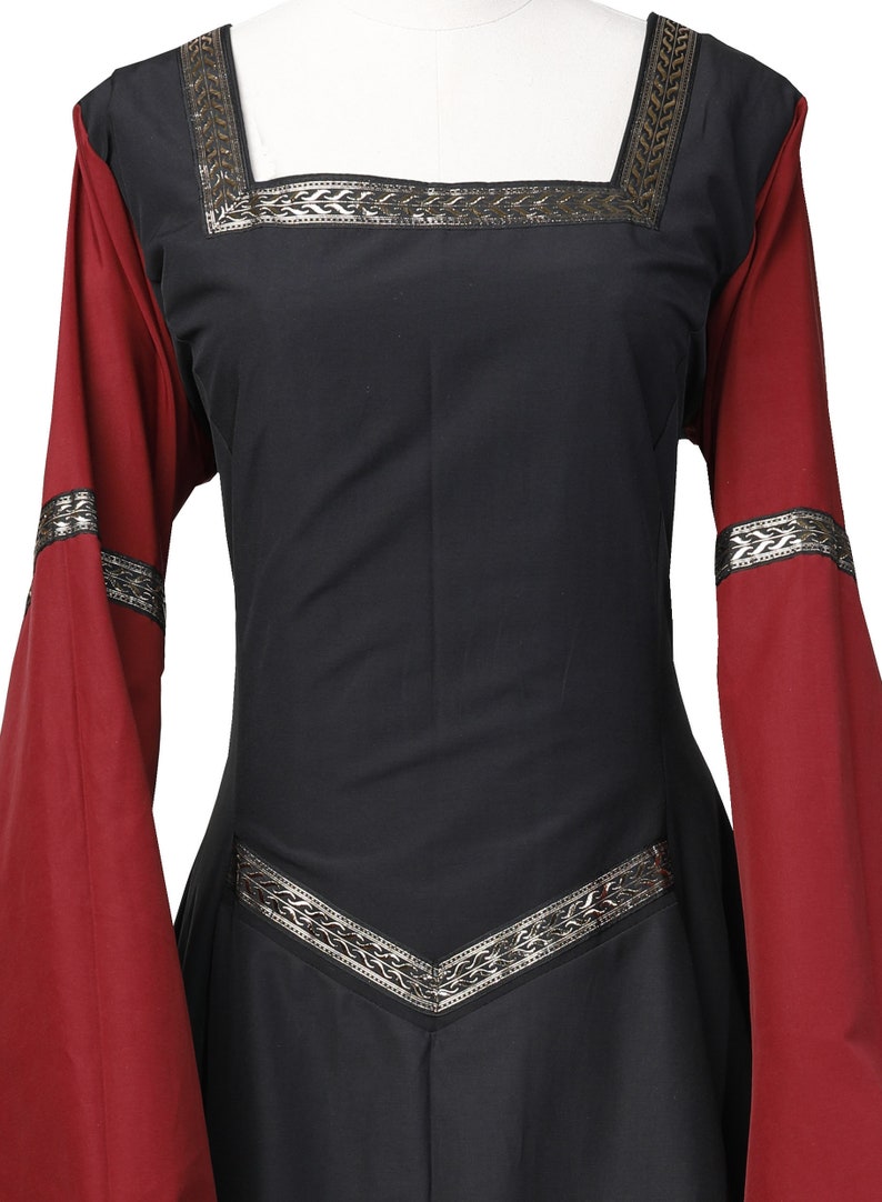 Puede incluir: Un vestido negro de estilo medieval con mangas largas. Las mangas son rojas con ribetes plateados. El vestido tiene ribetes plateados alrededor del escote y la cintura.