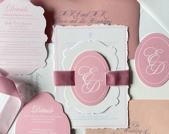 May include: Elegant wedding stationery set in shades of pink and white. Includes invitations, details cards, and envelopes with calligraphy. A pink ribbon wraps around the main invitation, which features the initials "ED".