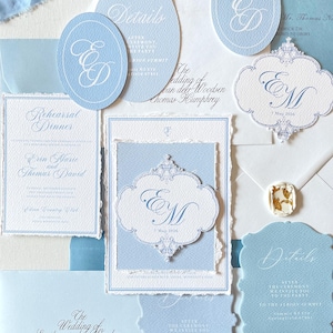 Puede incluir: Una colección de papelería de boda azul claro, que incluye invitaciones y tarjetas de confirmación de asistencia. Las invitaciones presentan una escritura elegante y bordes decorativos. Una cinta azul claro añade un toque delicado.