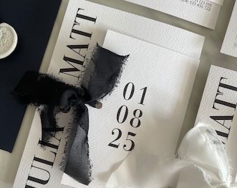 May include: Elegant wedding invitation suite featuring white cards with black text, including names and a date. A black ribbon and a navy envelope are also present. The suite includes contact information. The overall aesthetic is minimalist and modern.