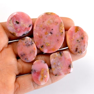 May include: Six pink and white oval-shaped gemstones with gold flecks. The gemstones are smooth and polished.