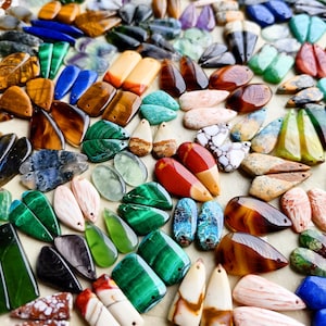 May include: A large collection of polished gemstone pendants in various shapes and colors, including malachite, tiger's eye, lapis lazuli, jasper, and agate. Each piece features a small drilled hole at the top for stringing, showcasing natural patterns.
