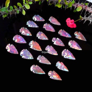 May include: A collection of 20 iridescent arrowhead shaped stones. The stones are a mix of pink, purple, and blue colors.