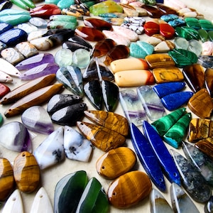 May include: A large collection of polished gemstone pendants in various shapes and colors, including tiger's eye, amethyst, malachite, lapis lazuli, and agate. Each piece features a small drilled hole for stringing, showcasing natural patterns.