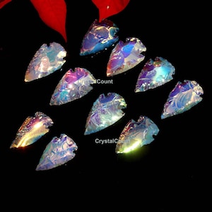 May include: A selection of iridescent glass arrowhead pendants. Each arrowhead has a unique shape and colour variations, with hues of blue, purple, and gold. The pendants are displayed against a black background, highlighting their shimmering qualities.