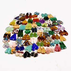 May include: A large collection of assorted polished gemstone cabochons in various shapes, colors, and patterns. The stones include teardrop, oval, and leaf-shaped pieces in shades of green, blue, brown, purple, red, and white, arranged in a loose cluster.