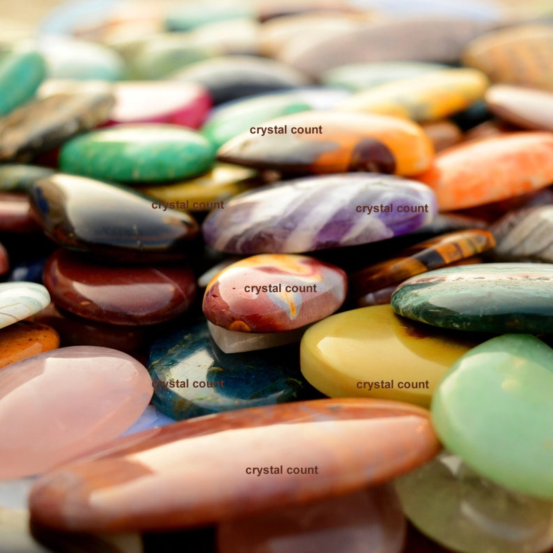 May include: A close-up of a variety of polished gemstone cabochons in various colours and patterns. The cabochons are arranged in a random pattern and are all different sizes and shapes.
