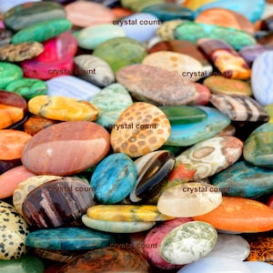 May include: A collection of colourful, oval-shaped gemstones. The stones are arranged in a random pattern and are of various sizes. The stones are all polished and have a smooth, shiny surface.