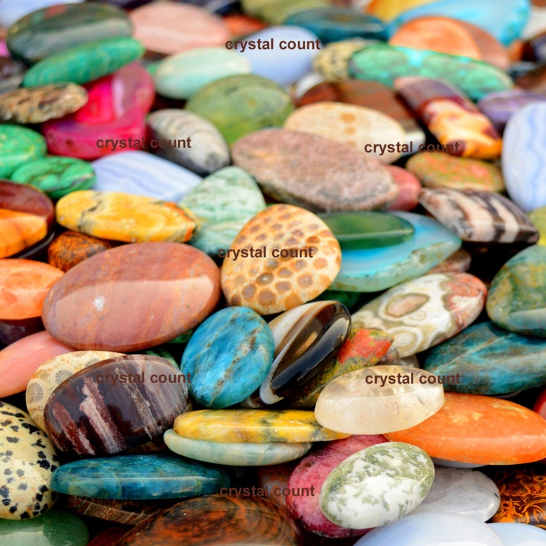 May include: A collection of colourful, oval-shaped gemstones. The stones are arranged in a random pattern and are of various sizes. The stones are all polished and have a smooth, shiny surface.