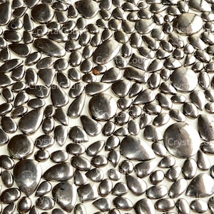 May include: A close-up view of a surface covered in numerous polished, dark gray river stones. The stones vary in size and shape, creating a textured, organic pattern. The stones have a reflective, glossy finish.