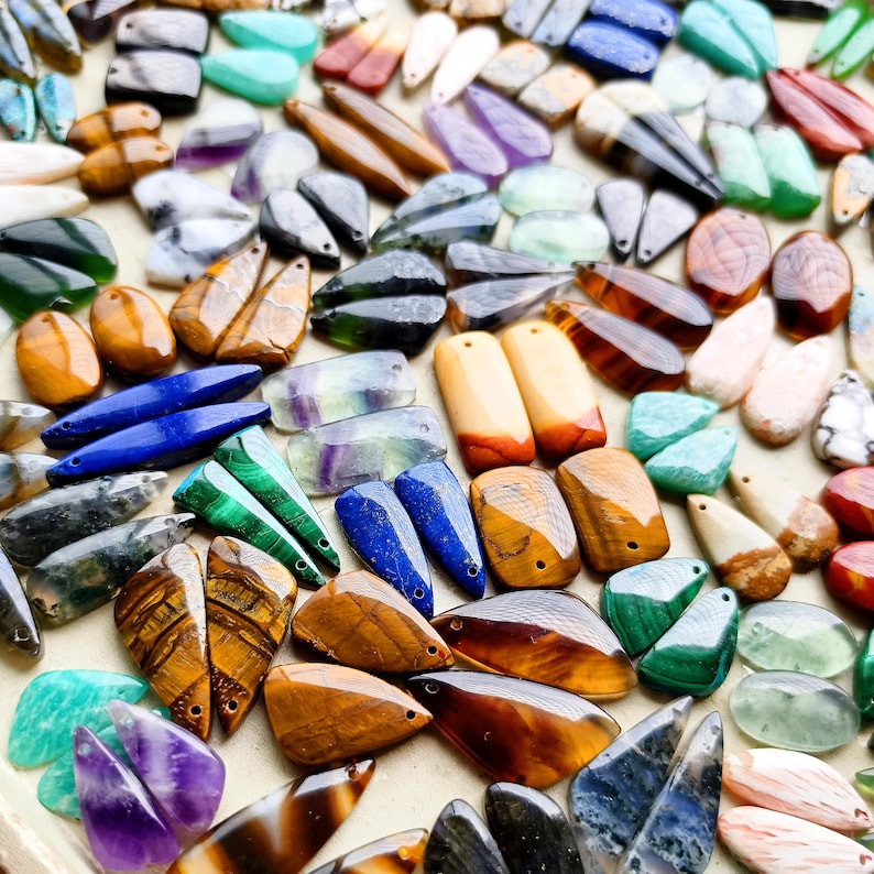 May include: A large collection of assorted gemstone pendants in various shapes and colors, including tiger eye, lapis lazuli, malachite, amethyst, and quartz. Each piece features a small drilled hole for stringing, showcasing natural stone textures.