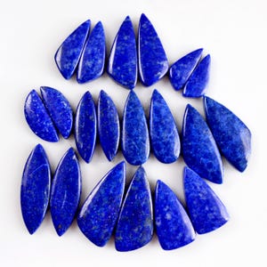 Könnte beinhalten: Eine Sammlung von 17 tropfenförmigen Lapislazuli-Cabochons. Die Steine sind tiefblau mit goldenen Pyrit-Einschlüssen.