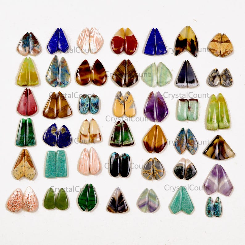 May include: A collection of assorted gemstone cabochons arranged in a grid, featuring various shapes, colors, and patterns including blue, green, brown, purple, and pink stones. Each pair of stones is polished and smooth, displaying natural mineral textures.