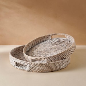 May include: Two white wicker trays with handles. The larger tray is stacked on top of the smaller tray.