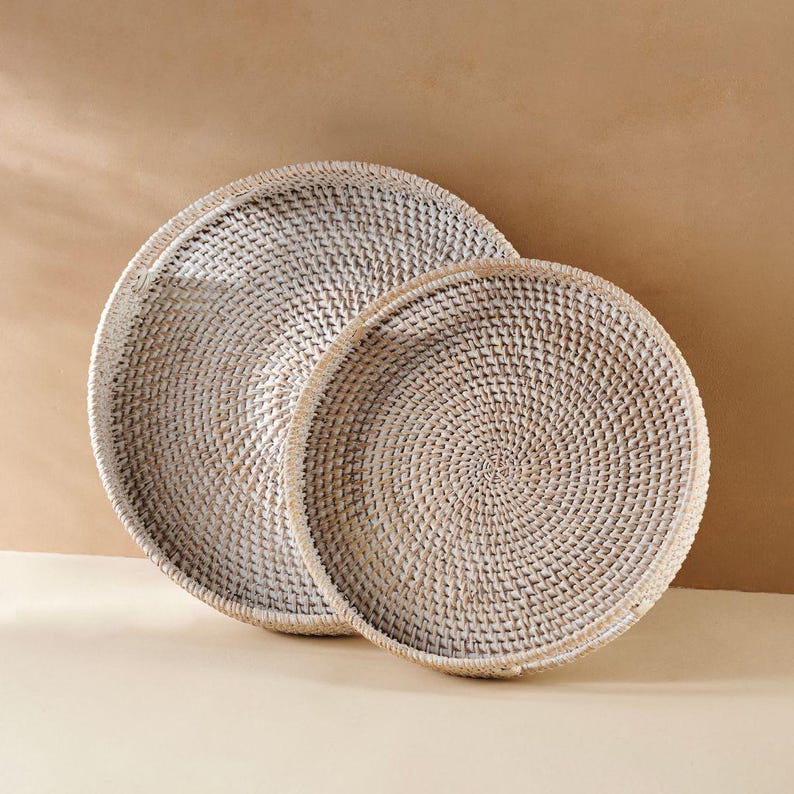 May include: Two white wicker trays, one nested inside the other. The trays are round and have a woven pattern.
