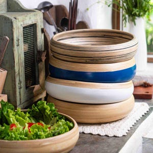 Könnte beinhalten: Ein Stapel aus vier Holzschalen mit natürlichem Finish, eine mit blauem Band und eine weitere mit weißem Band. Eine fünfte Schale enthält einen Salat mit Salat und Tomaten.
