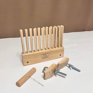 Op de afbeelding: Een houten weefgetouw met een houten shuttle, twee houten klemmen en twee metalen schroeven. Het weefgetouw heeft een label met de tekst "Weave Craft".