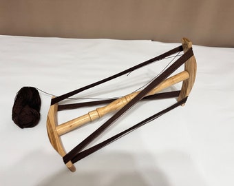 May include: A wooden yarn swift with brown yarn wound around it. The swift has a wooden spindle and is supported by four brown cords.